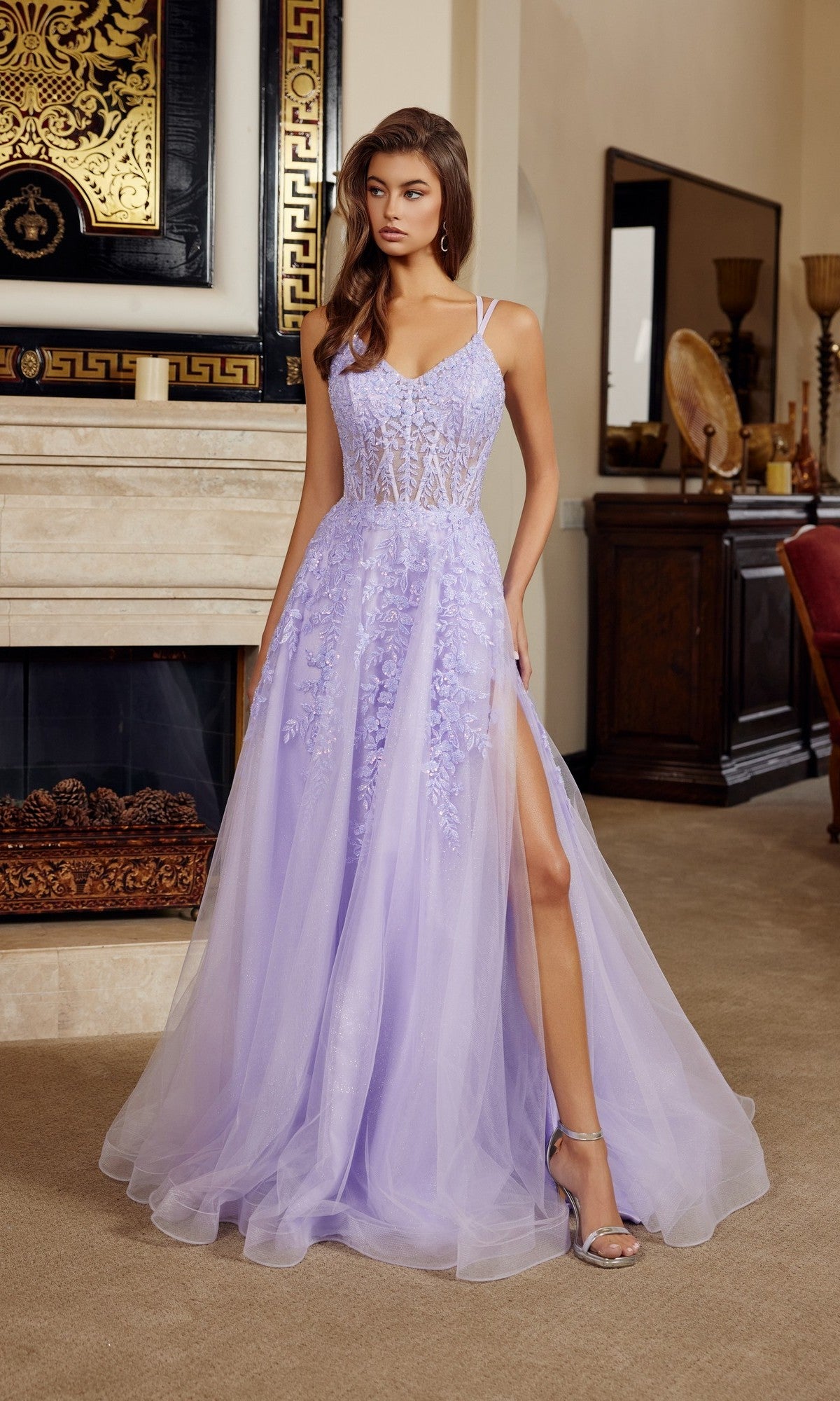 A woman stands indoors wearing the Nox Anabel H1882, a pastel long prom dress with floral details, a sheer bodice, tulle A-line skirt, and a thigh-high slit.